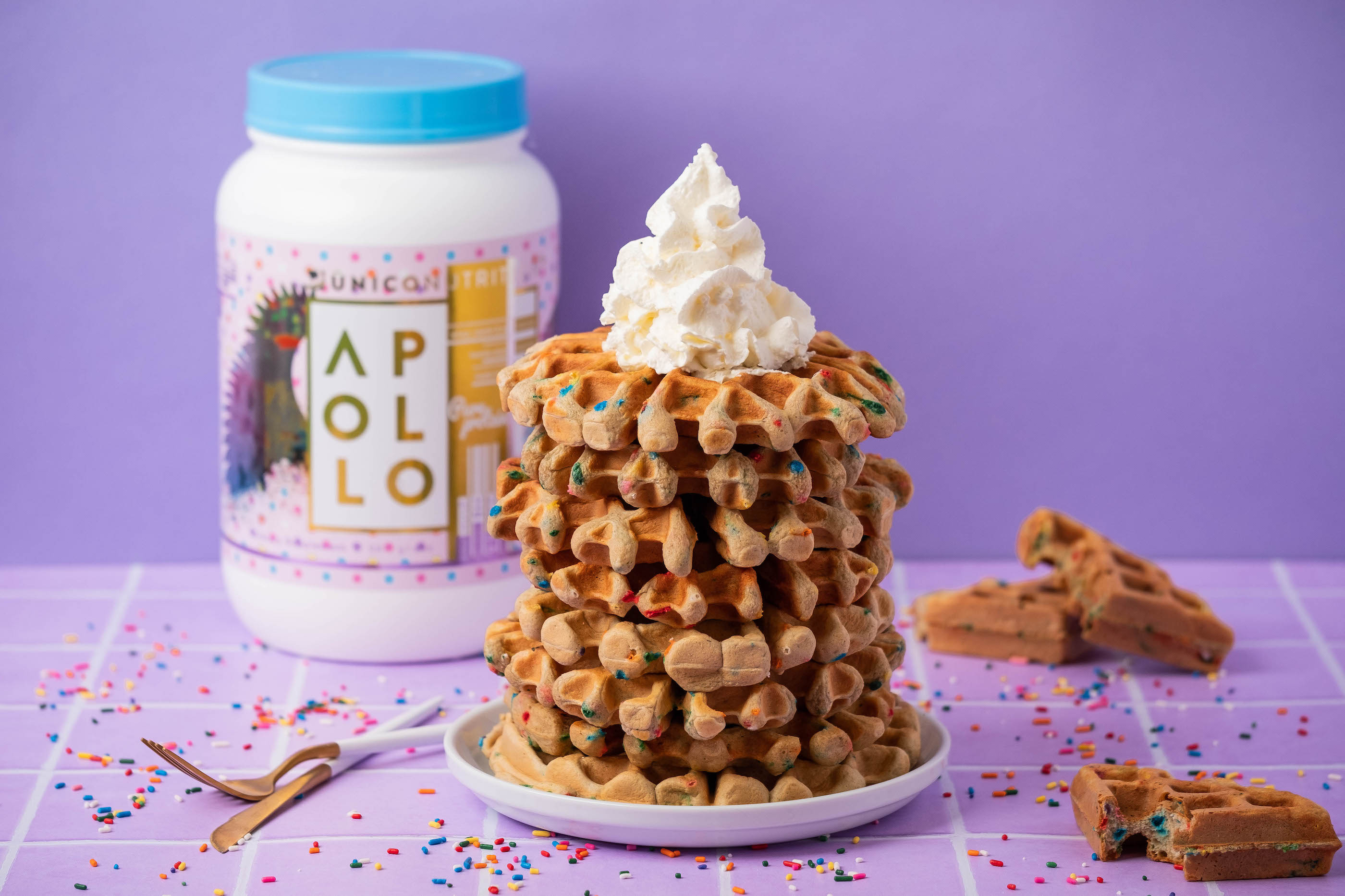 A stack of protein waffles made with birthday cake protein powder, with protein powder jar in background. Abstract purple scenery.