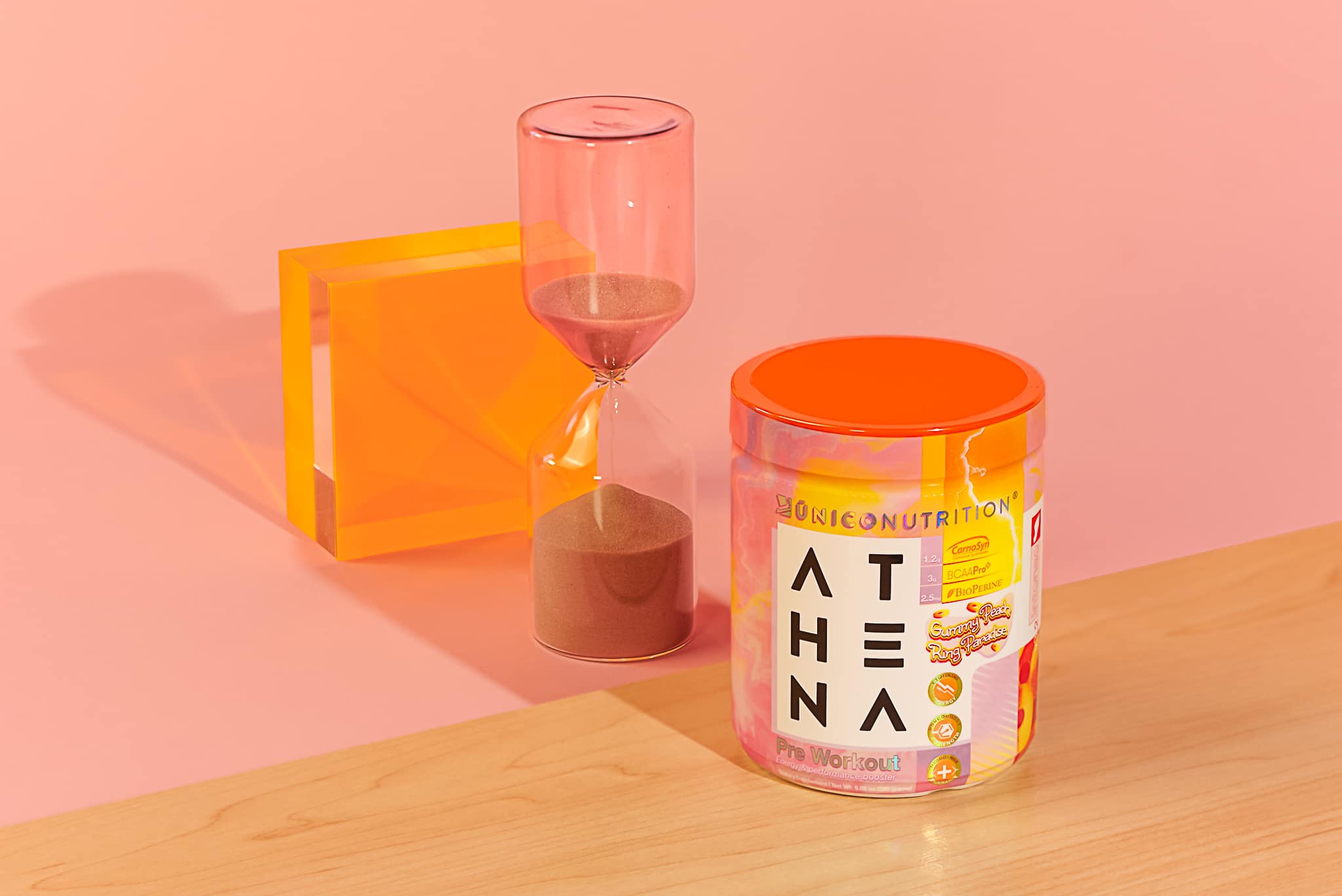 jar of peach flavored pre workout on plywood table with pink hourglass and orange plastic decoration