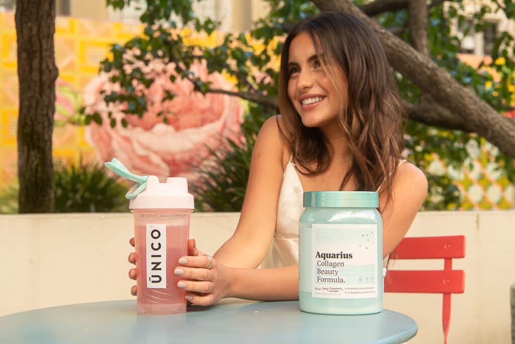 smiling woman in garden holding a shaker with collagen drink