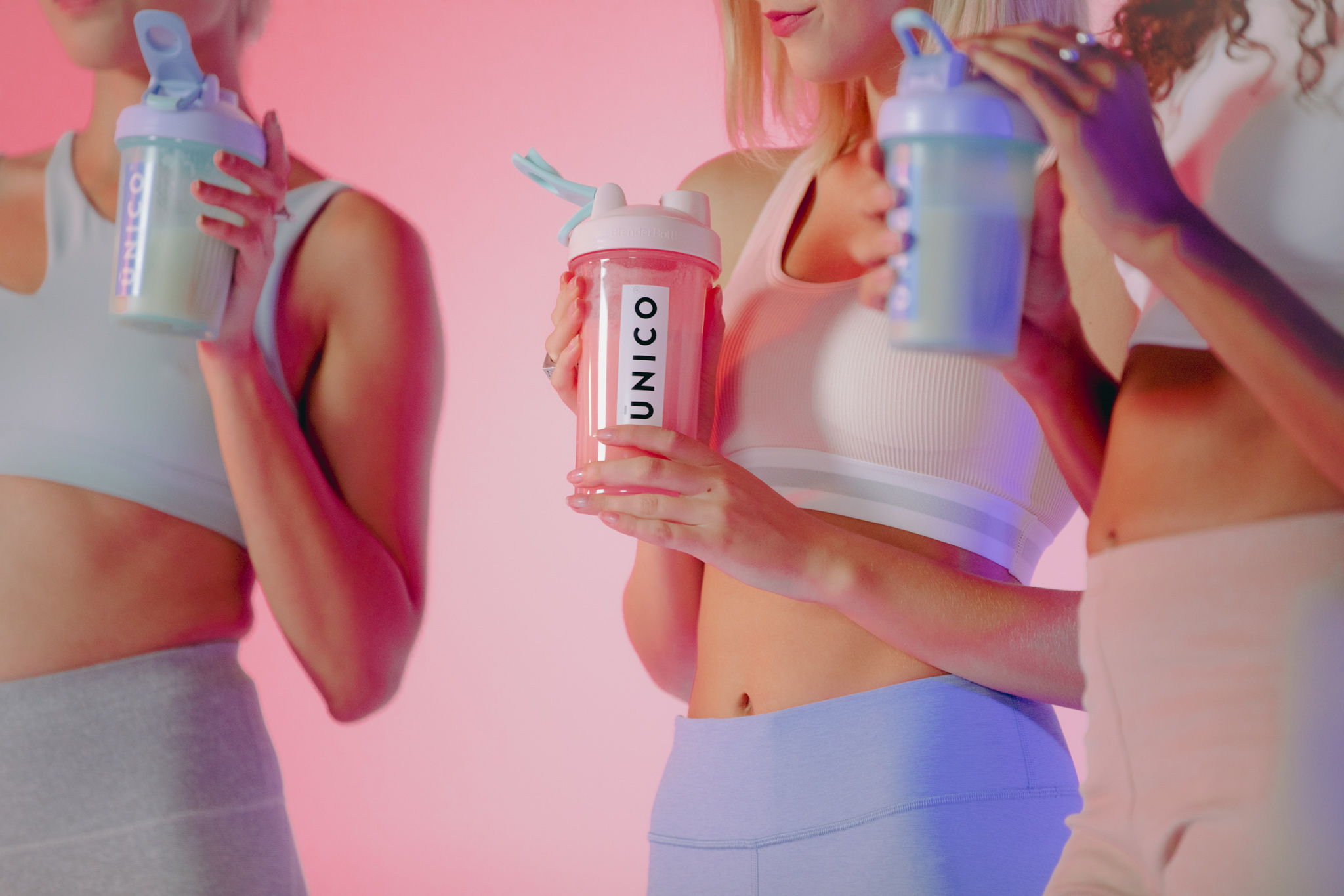 three woman drinking protein shakes in front of pink staged backdrop