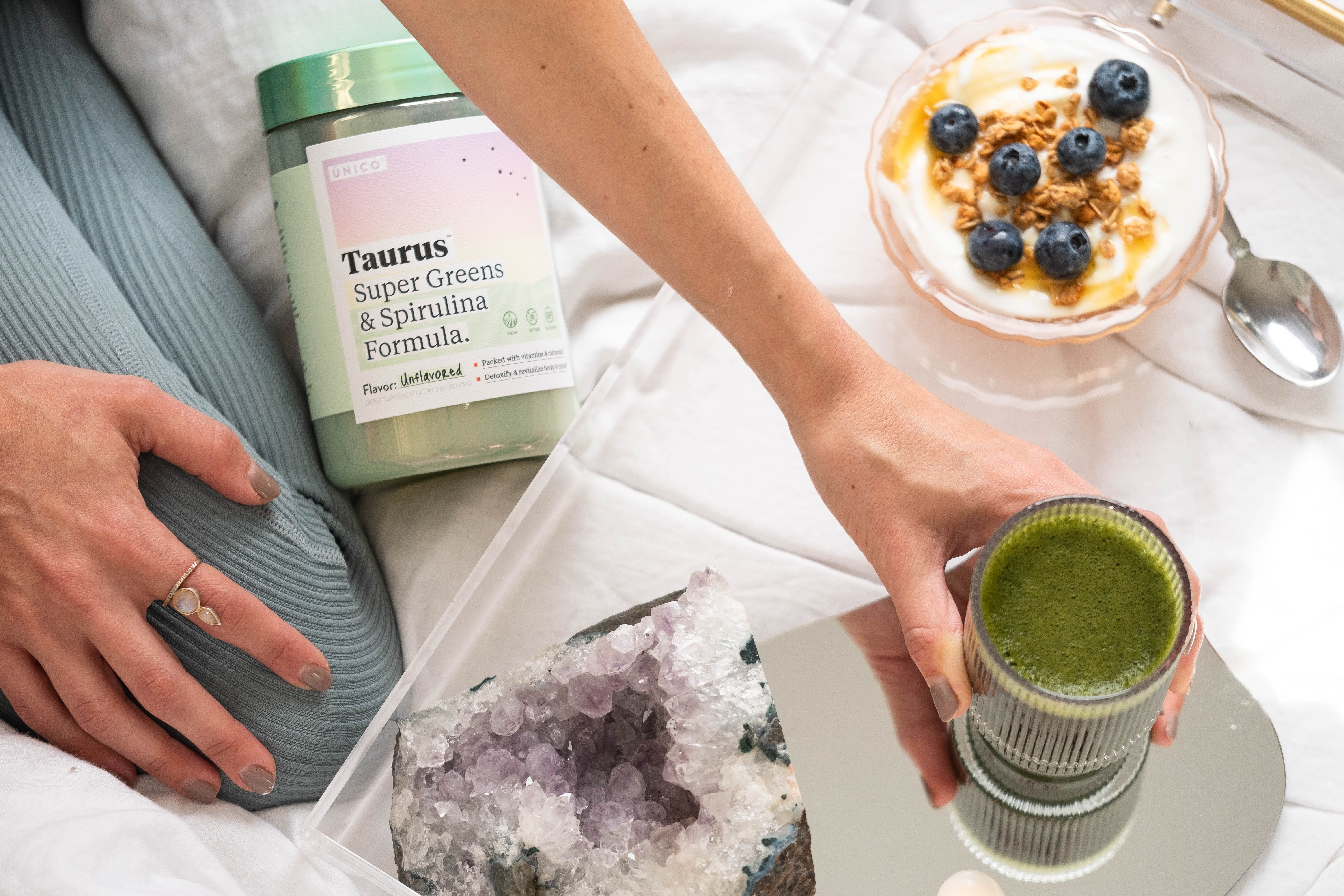 fit woman kneeling on bed, holding glass of algae superfood greens drink