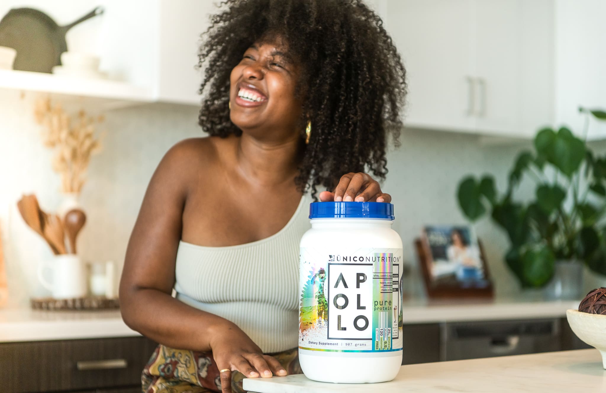 woman smiling in kitchen with jar of protein powder