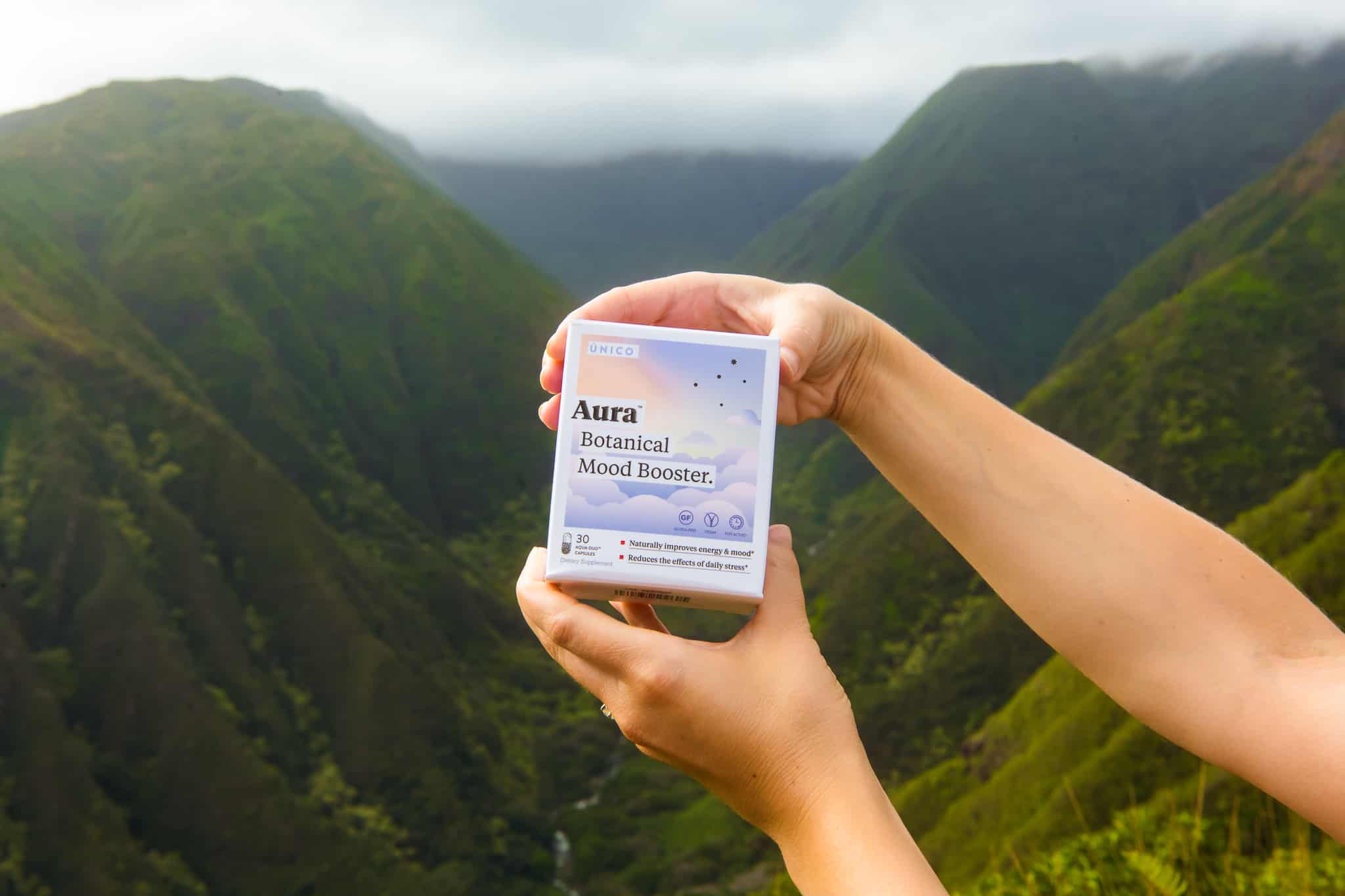 woman holding stress supplement in front of mountainous Hawaiian backdrop.