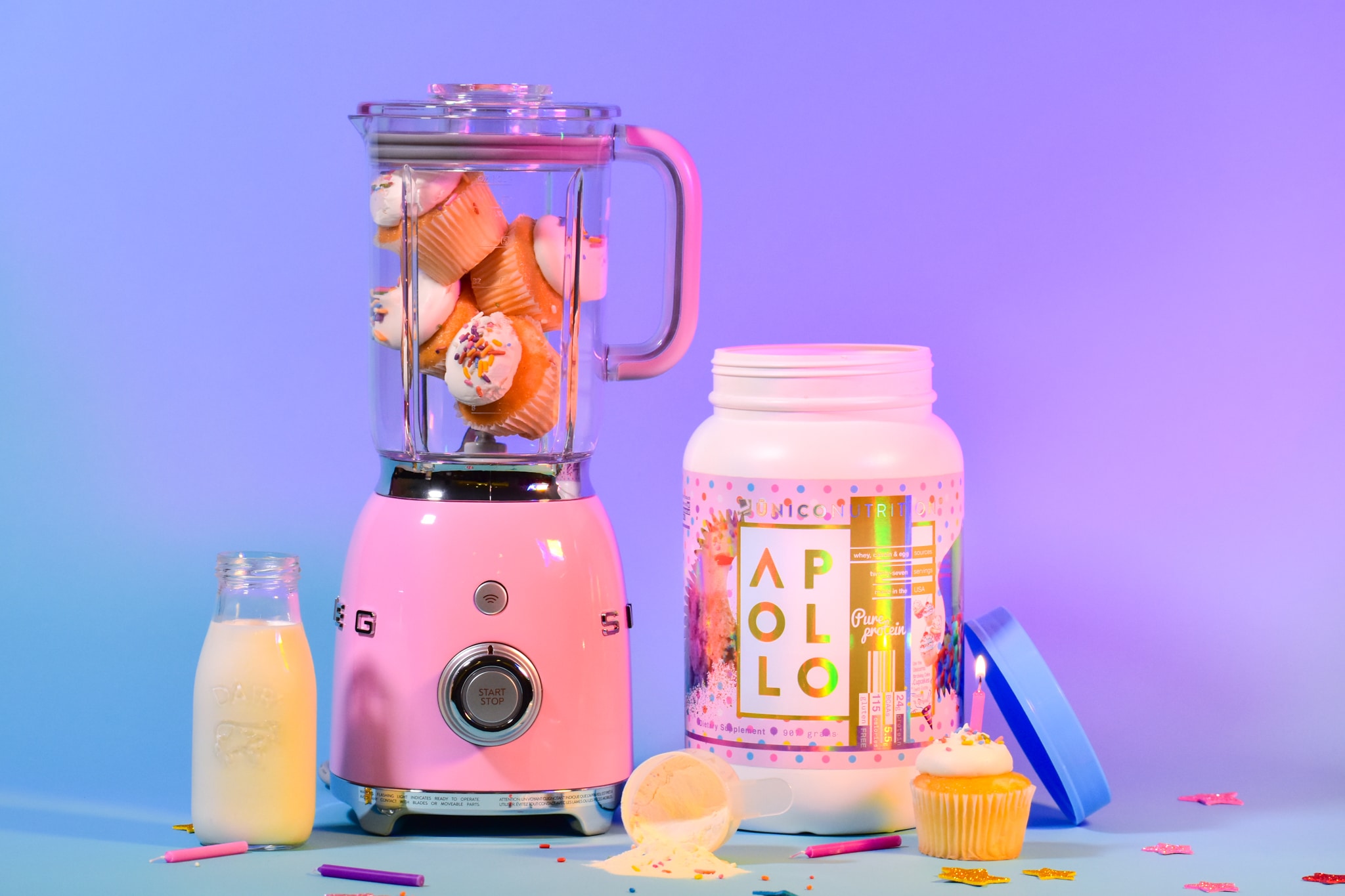 photo of a pink blender filled with birthday cake cupcakes, next to a jar of unico protein powder, with jar of milk and colorful blue and purple background.